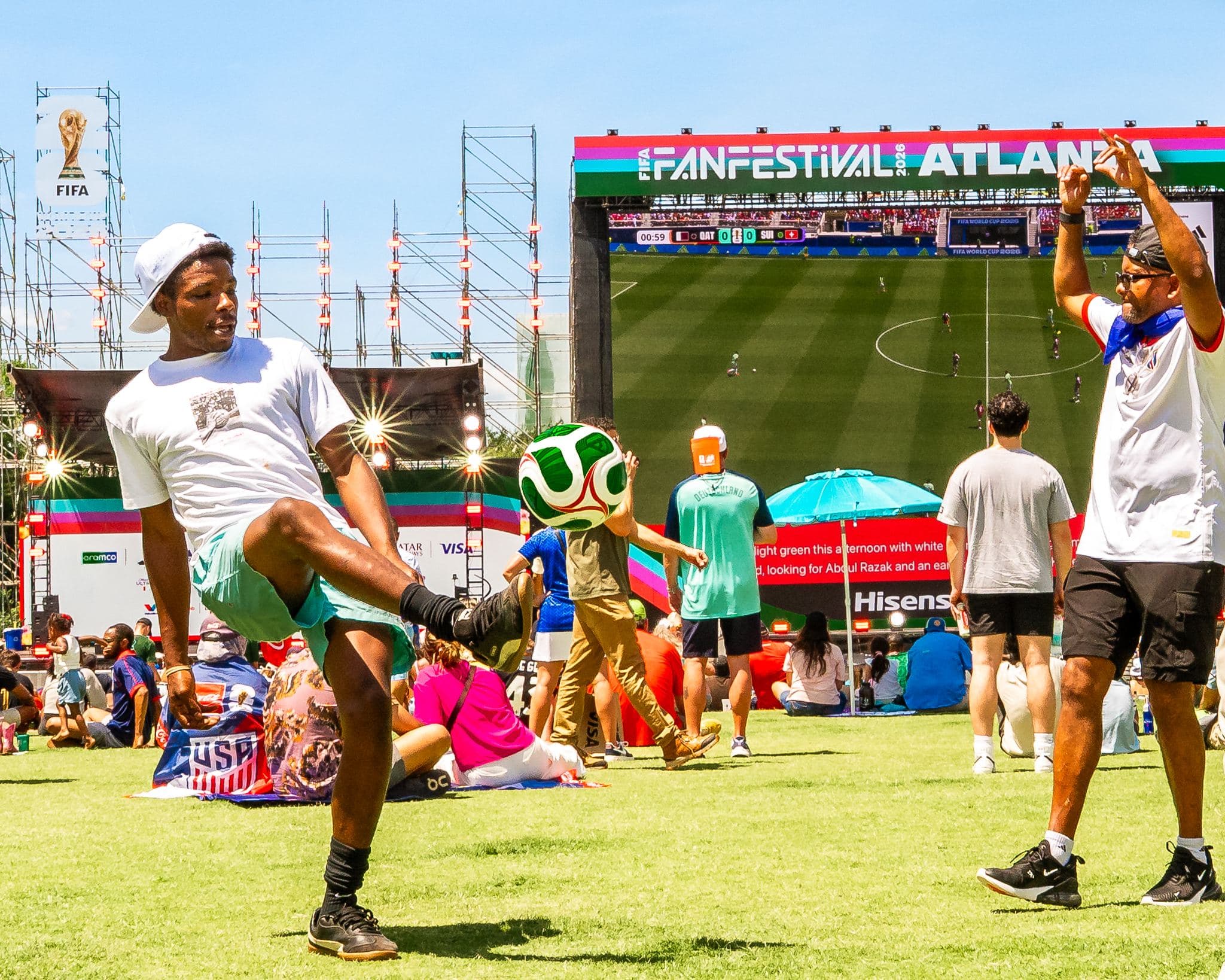 Fan juggling a soccer ball while another fan celebrates in front of the big screen at FIFA Fan Festival Atlanta