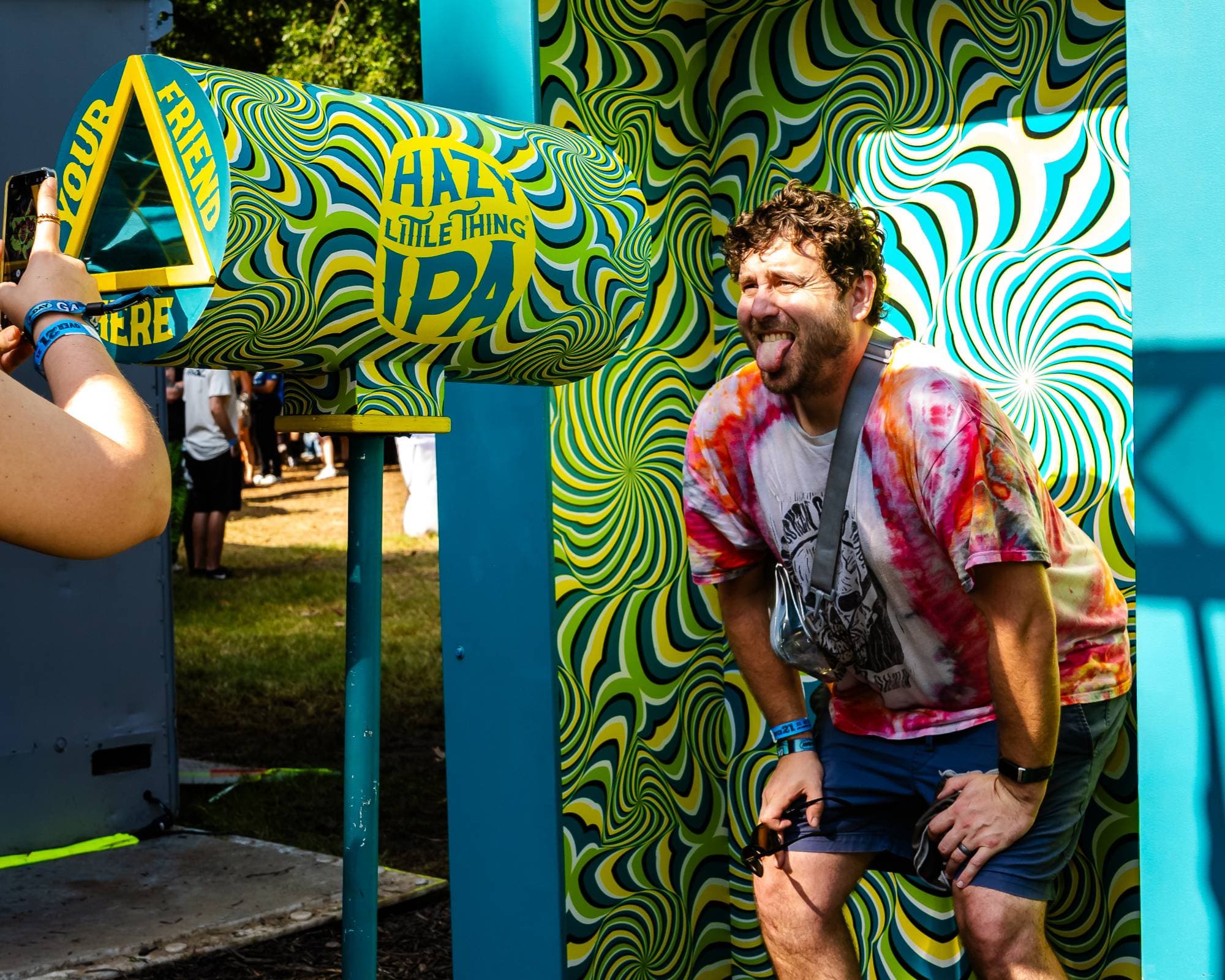 Festival goer sticking out his tongue at the Sierra Nevada Hazy Little Thing IPA optical illusion photo op with a swirling psychedelic backdrop