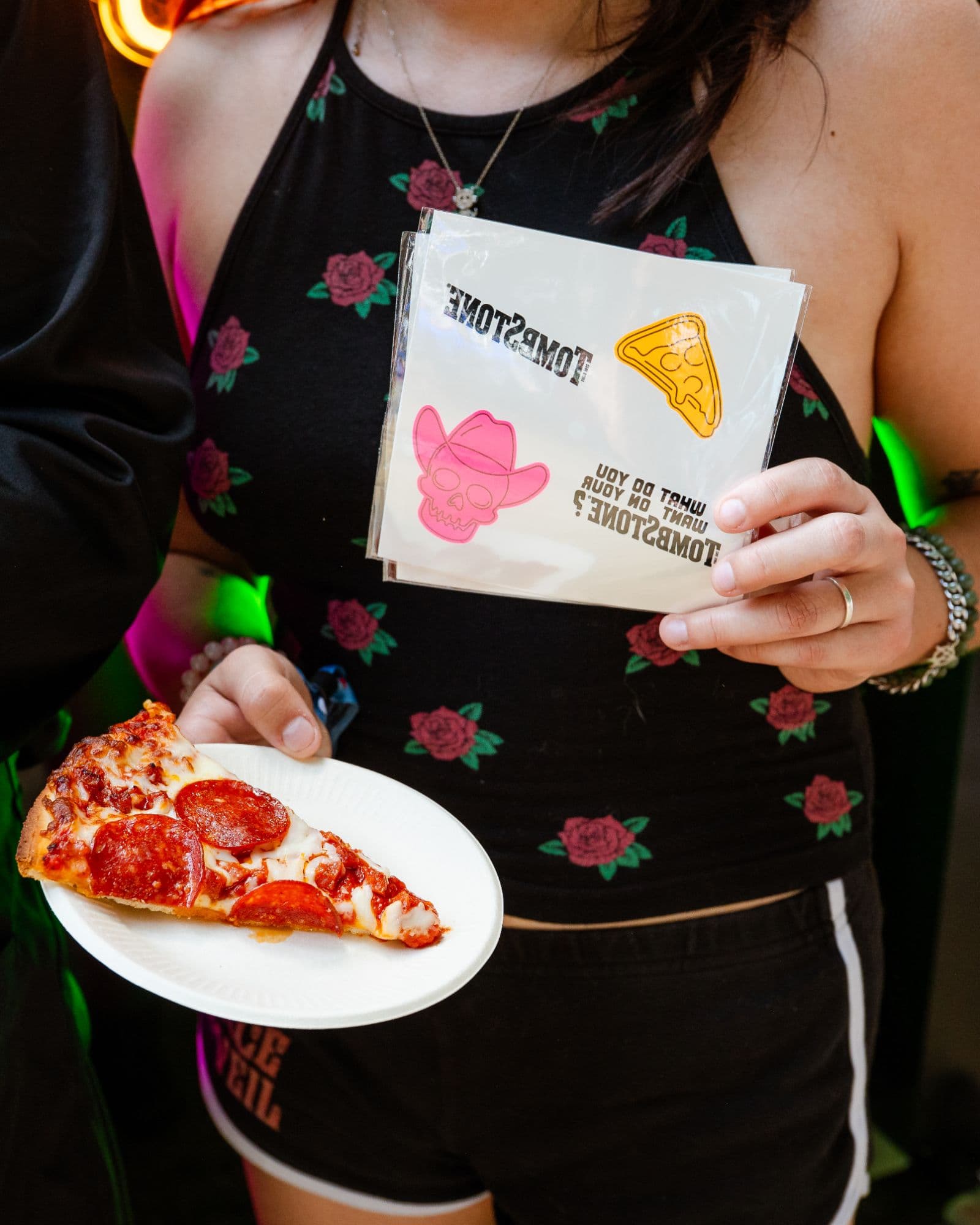 Festival goer holding a free slice of Tombstone pepperoni pizza and a sheet of Tombstone temporary tattoos at Shaky Knees